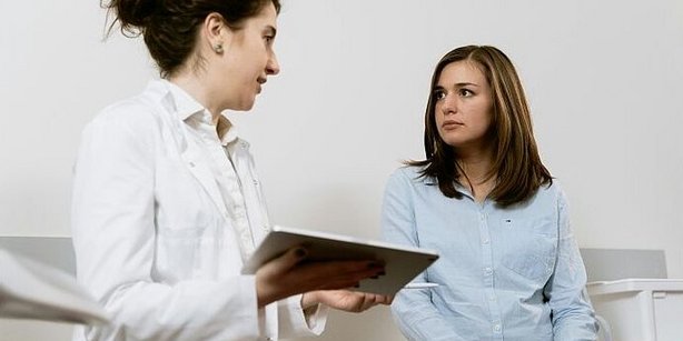 Zu sehen ist eine Ärztin und eine Patientin. Beide Personen befinden sich im Gespräch miteinander. Die Ärztin hält ein Tablet, auf Basis dessen sie ihre Erklärung fundiert.