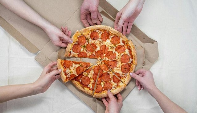 Zu sehen sind sechs Arme mit Händen, die nach einer Salami-Pizza im Zentrum des Bildes greifen.