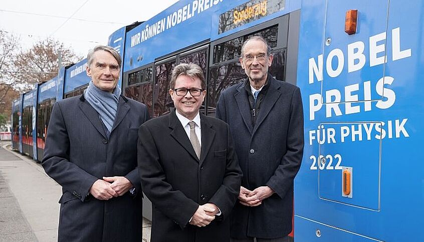 (c) derknopdruecker.com Rektor der Universität Wien Sebastian Schütze, Bildungsminister Pollaschek und ÖAW Präsident Fassman stehen vor der Nobelpreis-Bim.