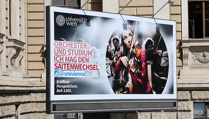 Billboard vor dem Hauptgebäude der Uni Wien mit dem Slogan: "Orchester und Studium: Ich mag den Saitenwechsel""