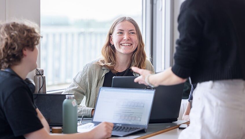 Student*innen Student*innen sitzen vor Laptops und unterhalten sich