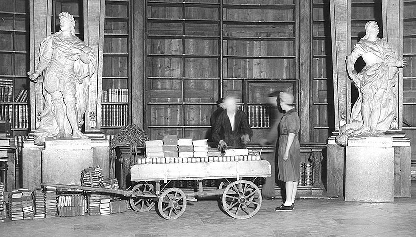 Auf dem schwarz-weiß Foto zu sehen wie Bücher aus dem Prunksaal in Schutzräume gebracht werden, um sie vor den Luftangriffen der Alliierten zu sichern.