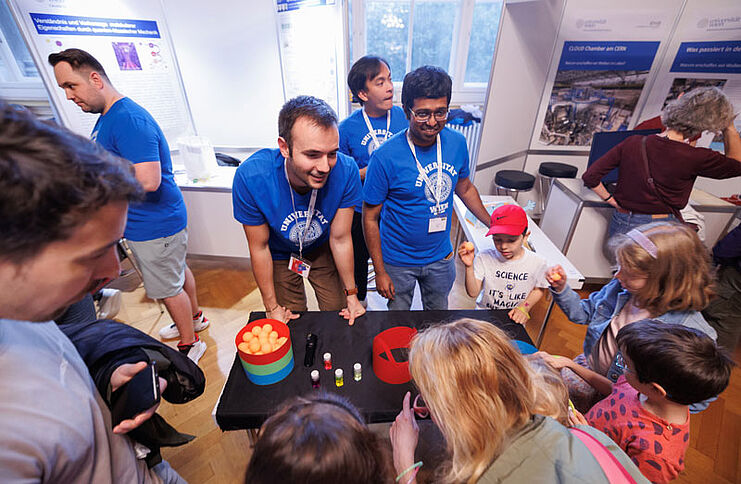 Physiker mit Besucher*innen bei einem Experiment