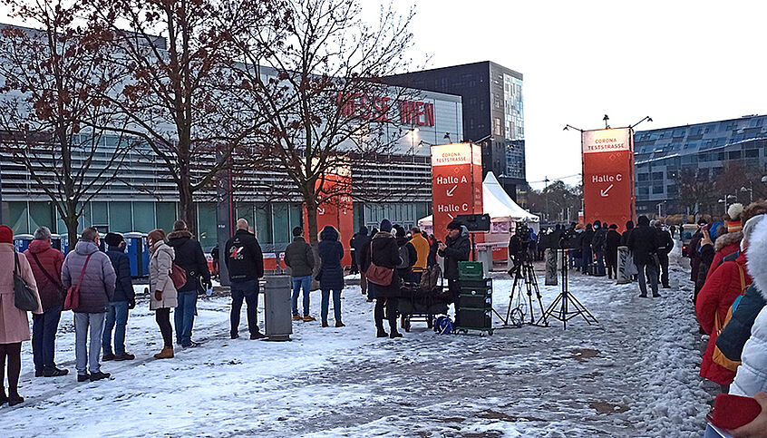 © Dr. Korom János via Wikipedia Menschen stehen im Schnee vor der Messe Wien an um auf das Coronavirus getestet zu werden.