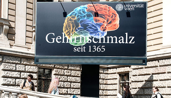 Plakatwand "Gehirnschmalz. Seit 1365" vor dem Hauptgebäude