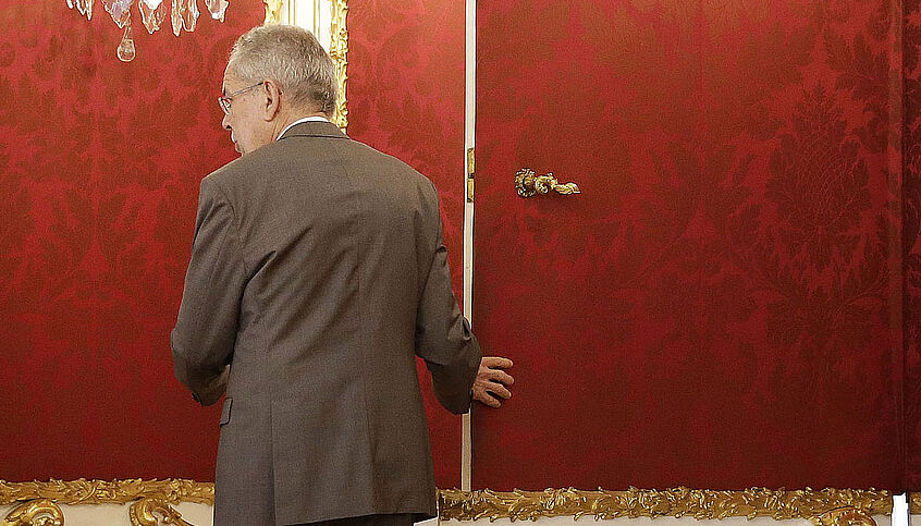 Bundespräsident van der Bellen geht durch die berühmte Tapetentür. Er zeigt der Kamera seinen Rücken