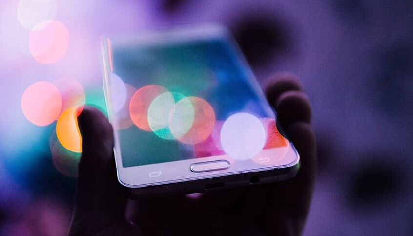 (c) unsplash Ein Handy wird von einer Hand gehalten, das Display ist unscharf.