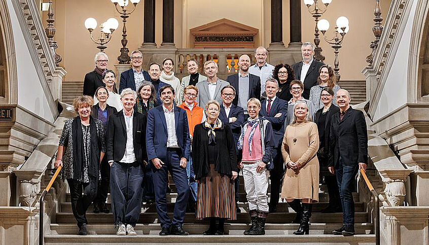 © Joseph Krpelan, Knopfdrücker 26 Personen posieren für ein Gruppenfoto auf der Prunkstiege der Universität Wien.