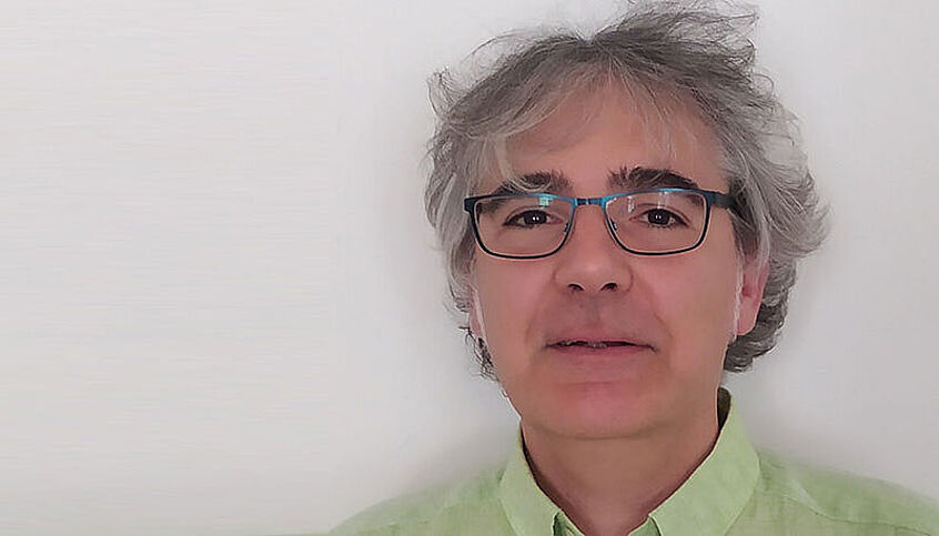 Der neue Professor für Algebraische Geometrie schaut in die Kamera. Er hat graue Haare, trägt eine Brille und trägt ein grünes Hemd.